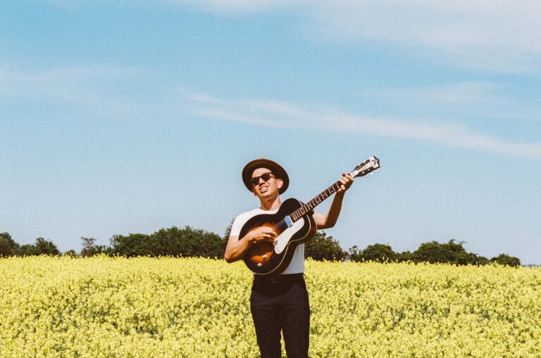 Man playing guitar in a field of flowers.