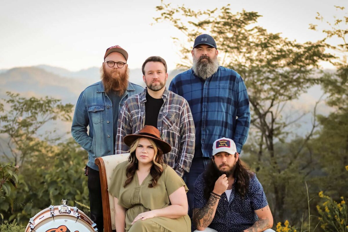 Outdoor portrait of five people posing with instruments and mountains in the background.