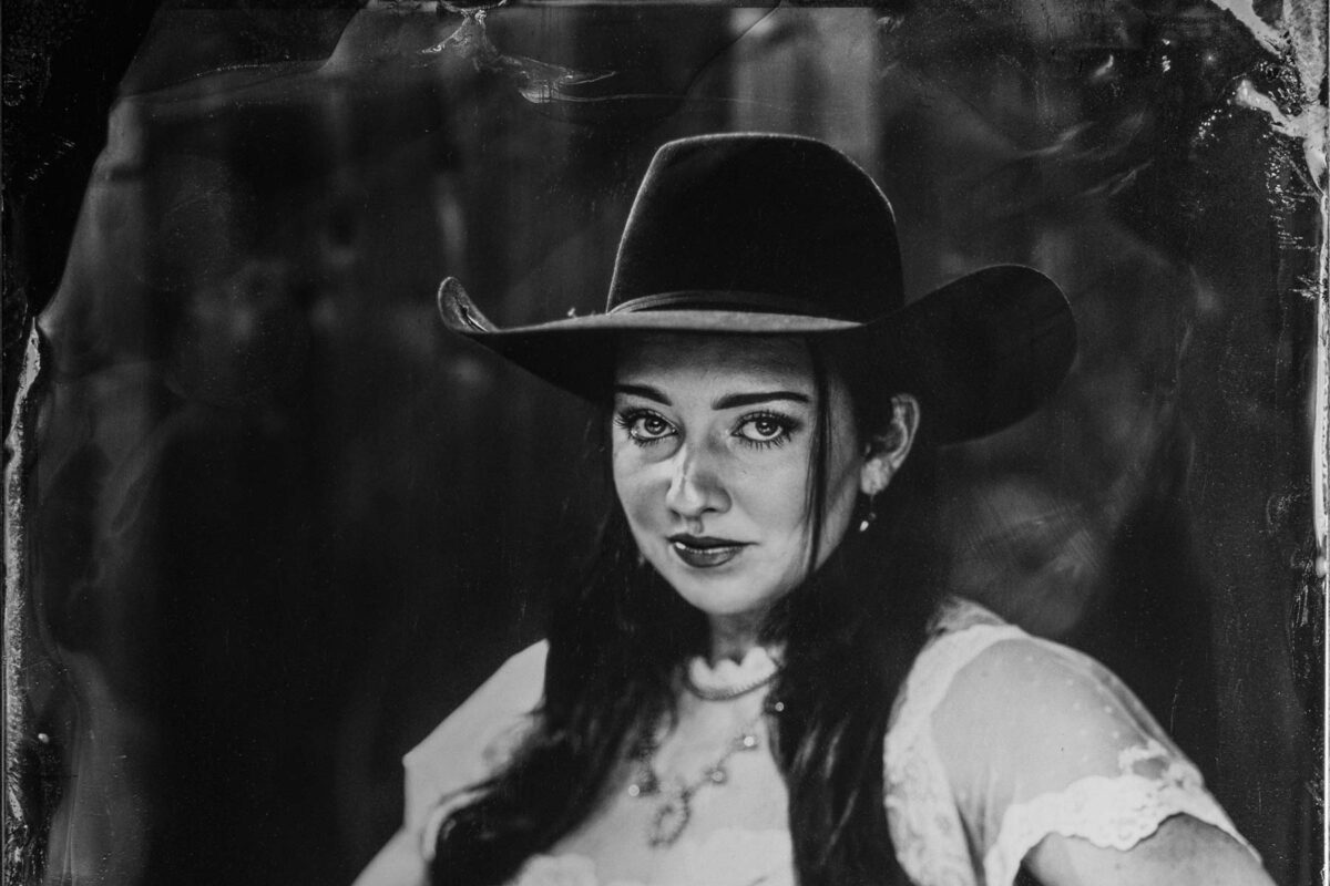 Woman in cowboy hat playing guitar.