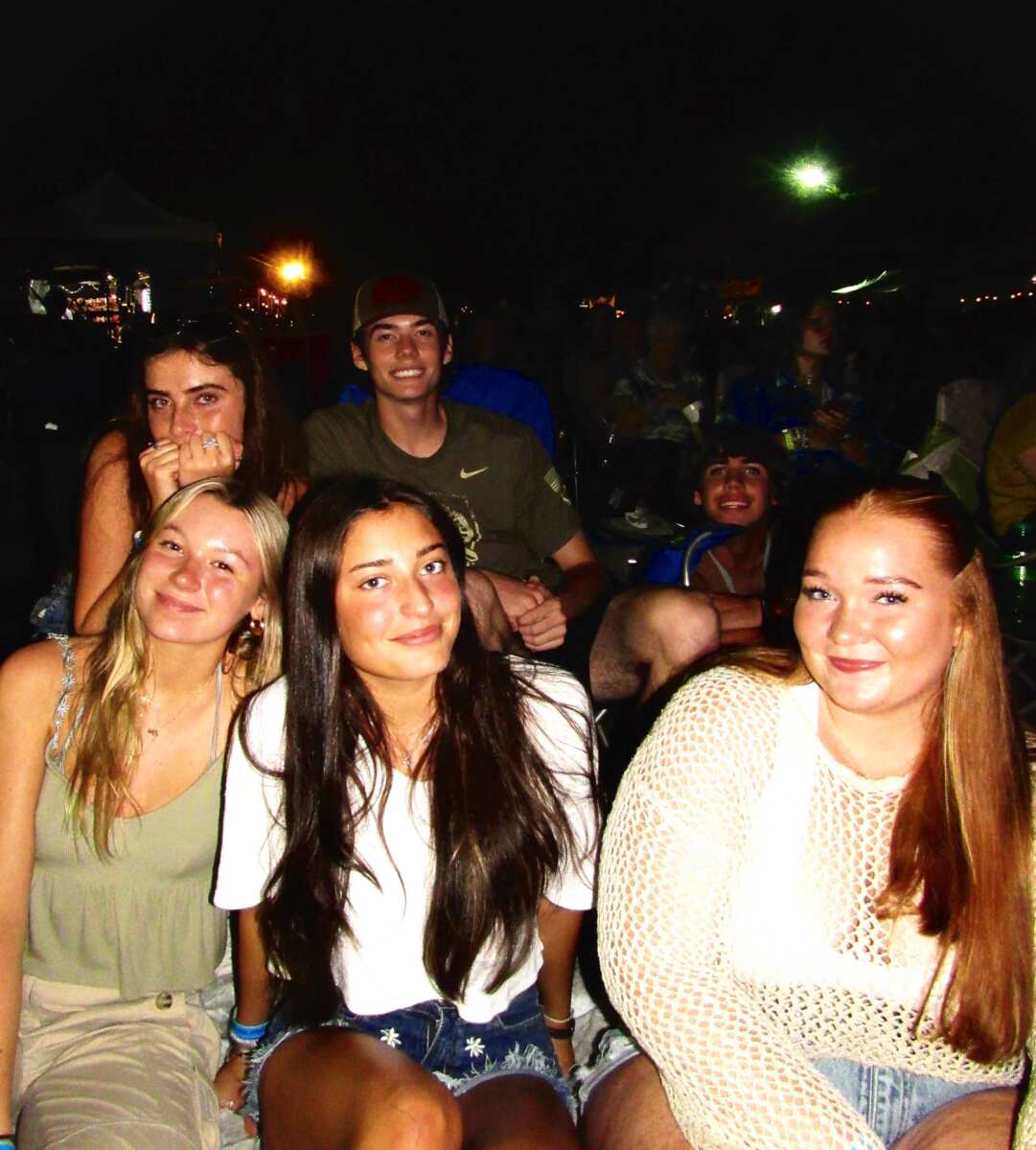 group of teenagers/young adults smiling and posing in outdoor concert setting at nighttime