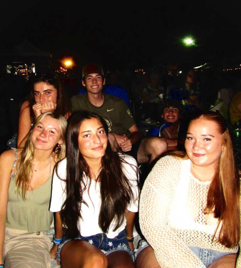 group of teenagers/young adults smiling and posing in outdoor concert setting at nighttime