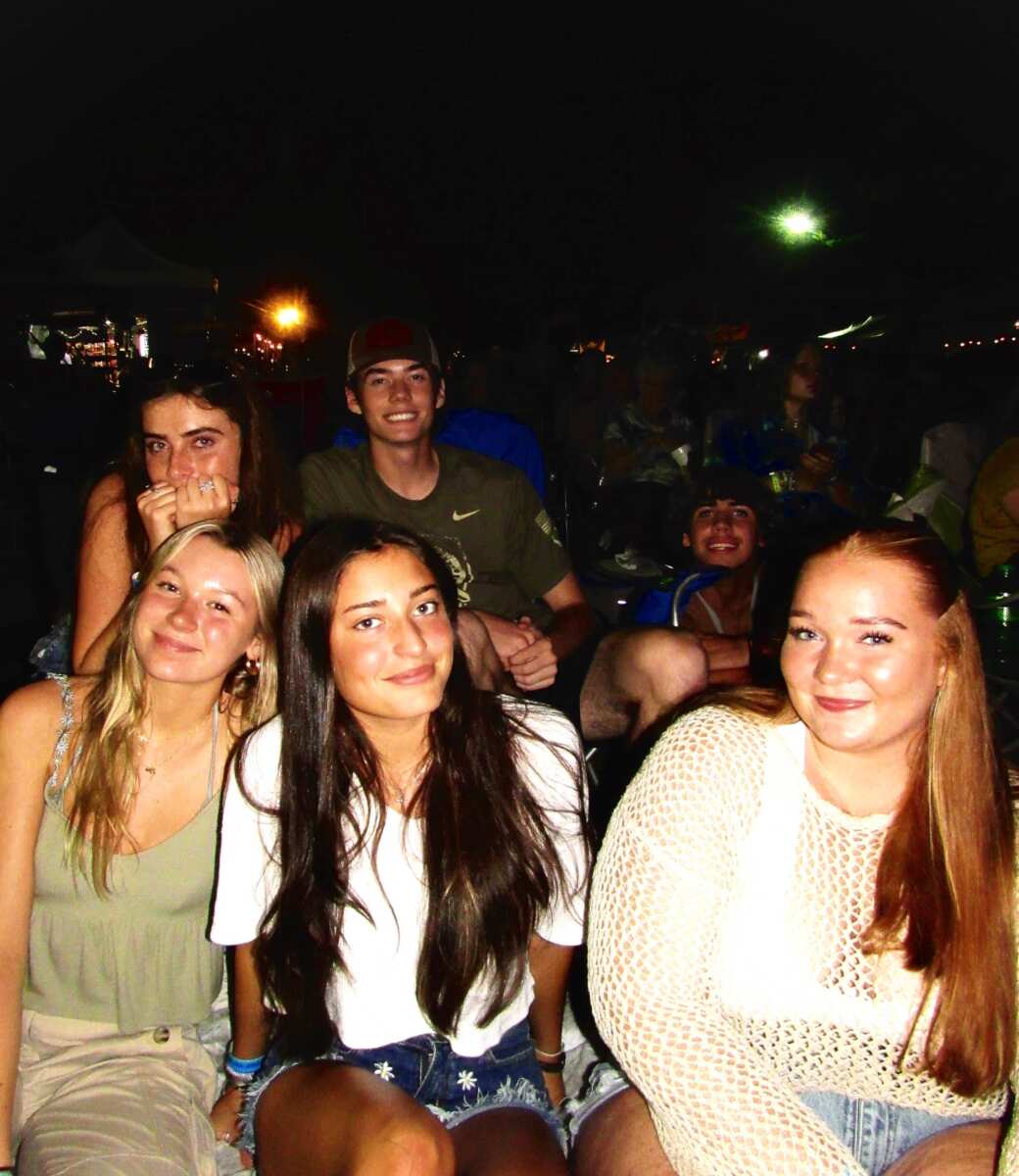 group of teenagers/young adults smiling and posing in outdoor concert setting at nighttime