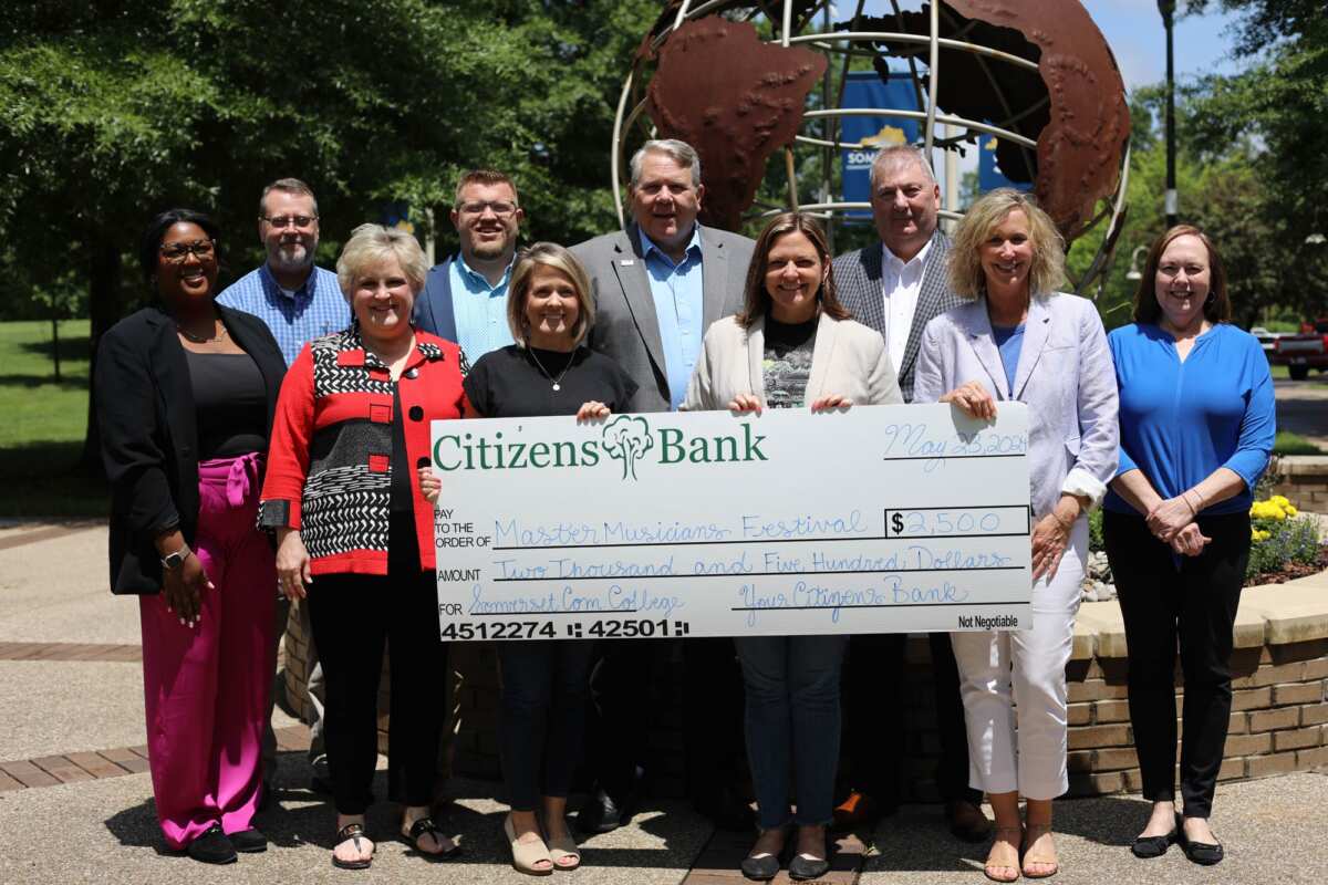 A group of people standing in front of globe sculpture outdoors smiling holding an oversized $2500 check from Citizens Bank