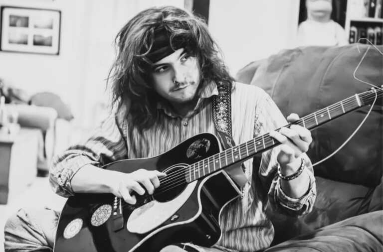 Drake Nasher - black and white photo of man sitting playing guitar