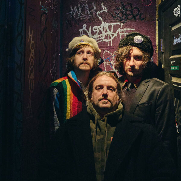 three band members in dark space with graffiti background