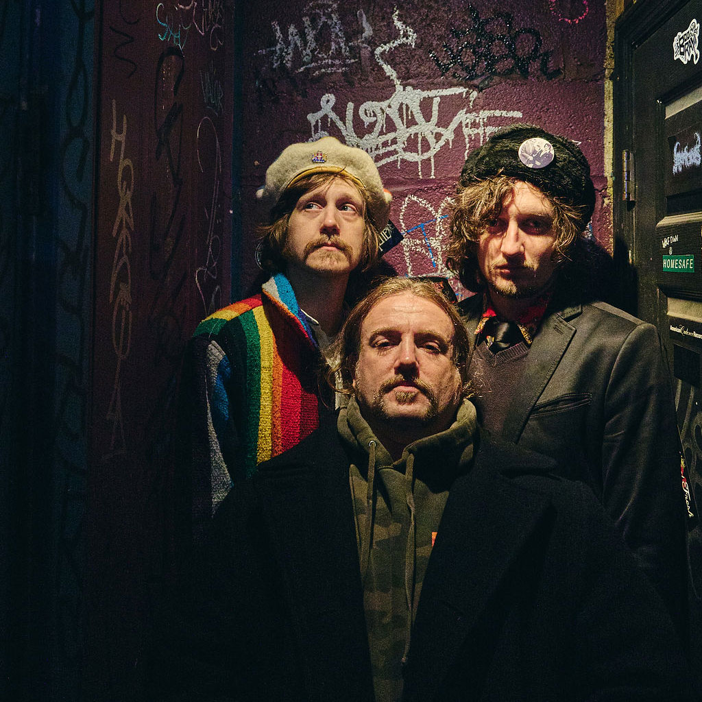three band members in dark space with graffiti background