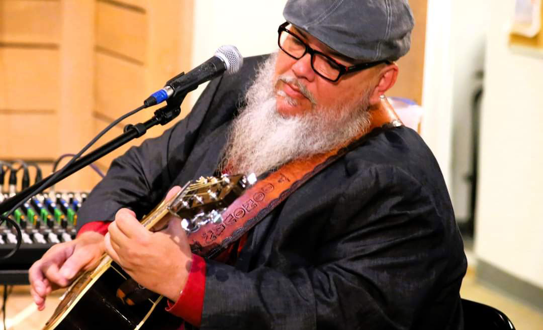 man with white beard and glasses playing acoustic guitar
