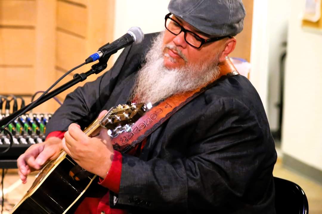 man with white beard and glasses playing acoustic guitar