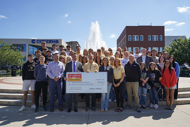 group of people standing on town square holding large donation check