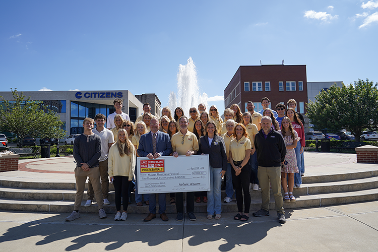 group of people standing on town square holding large donation check